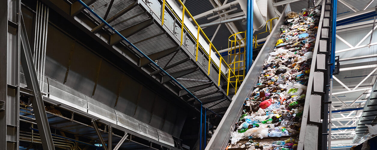 Conveyor belt with garbage transports waste inside drum filter or rotating cylindrical sieve with trommel for sorting pieces of garbage into various sizes fractions at waste recycling plant.