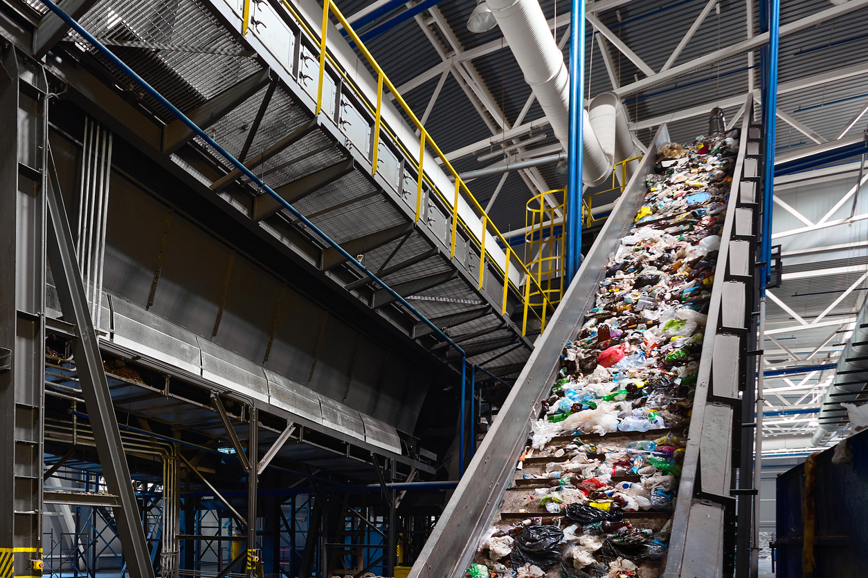 Conveyor belt with garbage transports waste inside drum filter or rotating cylindrical sieve with trommel for sorting pieces of garbage into various sizes fractions at waste recycling plant.