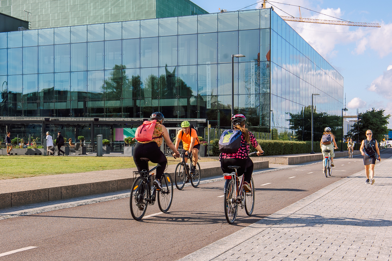 Helsinki, Finland - August 22, 2022: Cyclists in protective helmets ride along bike path in city center on Kansalaistori Square