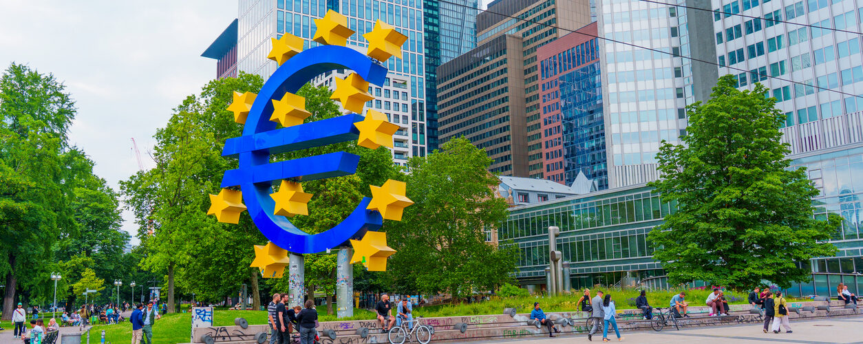 Frankfurt, Germany - June 10, 2025: Vibrant Euro symbol sculpture surrounded by lush greenery and contemporary skyscrapers in Frankfurt, capturing the essence of European finance.