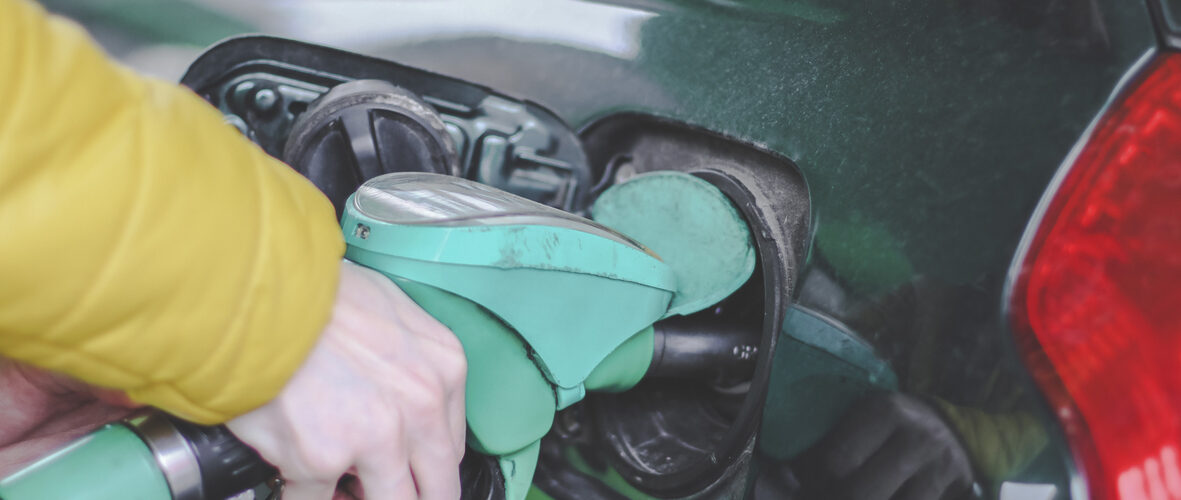The hand of a young caucasian man in a yellow jacket holds a gas station gun and refuels a car with gasoline at a city gas station, close-up side view. Gas station concept, service.