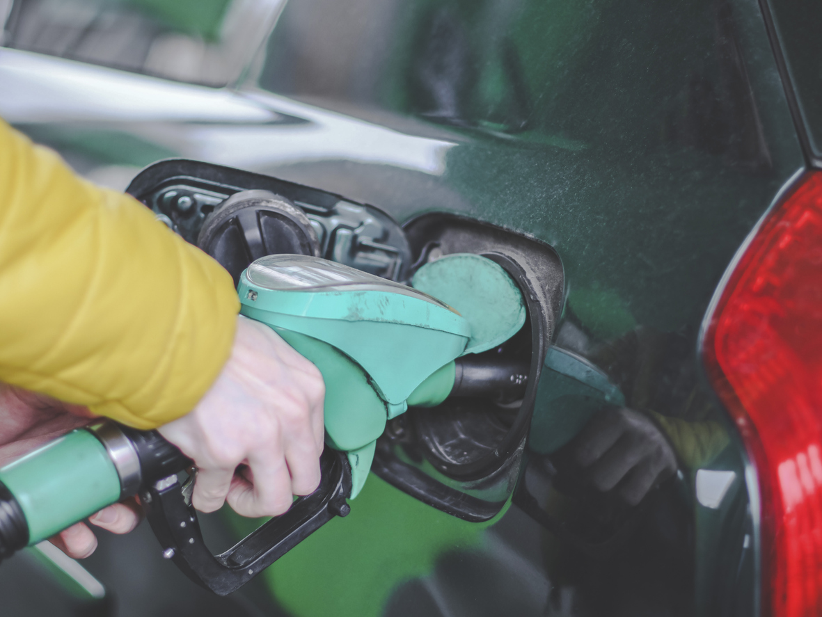 The hand of a young caucasian man in a yellow jacket holds a gas station gun and refuels a car with gasoline at a city gas station, close-up side view. Gas station concept, service.