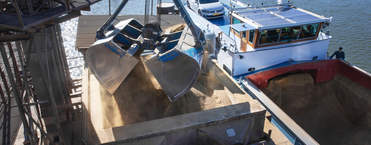 Unloading an inland barge filled with soja by crane. Transport by ship.