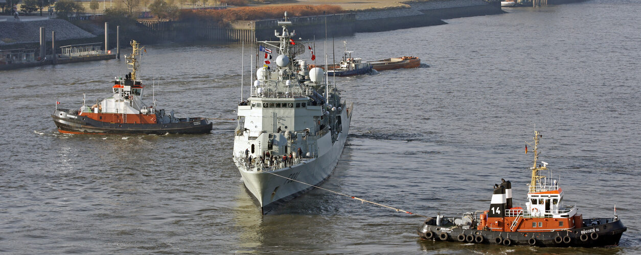 Hamburg, Germany - November 14, 2016: In Harbor help two tugs to reverse the direction of sailing one large military vessel in Hamburg