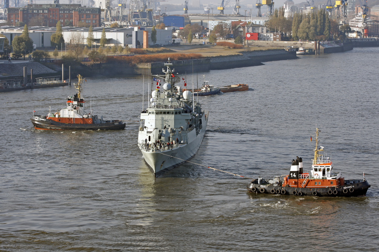 Hamburg, Germany - November 14, 2016: In Harbor help two tugs to reverse the direction of sailing one large military vessel in Hamburg