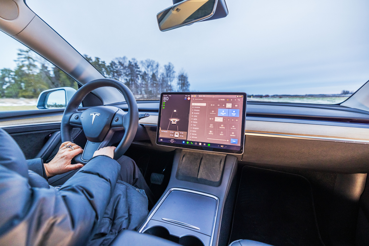 Sweden. Uppsala. 02.20.2025. Close-up view of driver holding steering wheel inside Tesla Model 3 electric car with touchscreen displaying vehicle controls.
