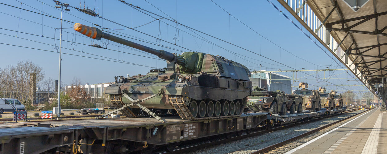 Military tanks and armored vehicles on freight train at railway station under clear blue sky, transportation. Hengelo, the Netherlands. 28 March 2025.