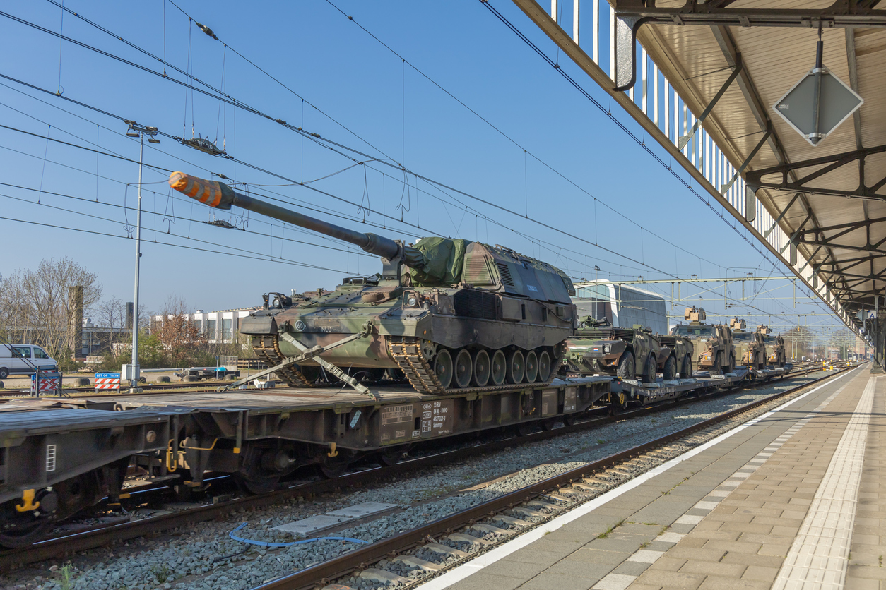 Military tanks and armored vehicles on freight train at railway station under clear blue sky, transportation. Hengelo, the Netherlands. 28 March 2025.