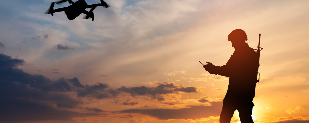 Silhouette of soldier are using drone and laptop computer for scouting during military operation against the backdrop of a sunset. Greeting card for Veterans Day, Memorial Day, Independence Day.