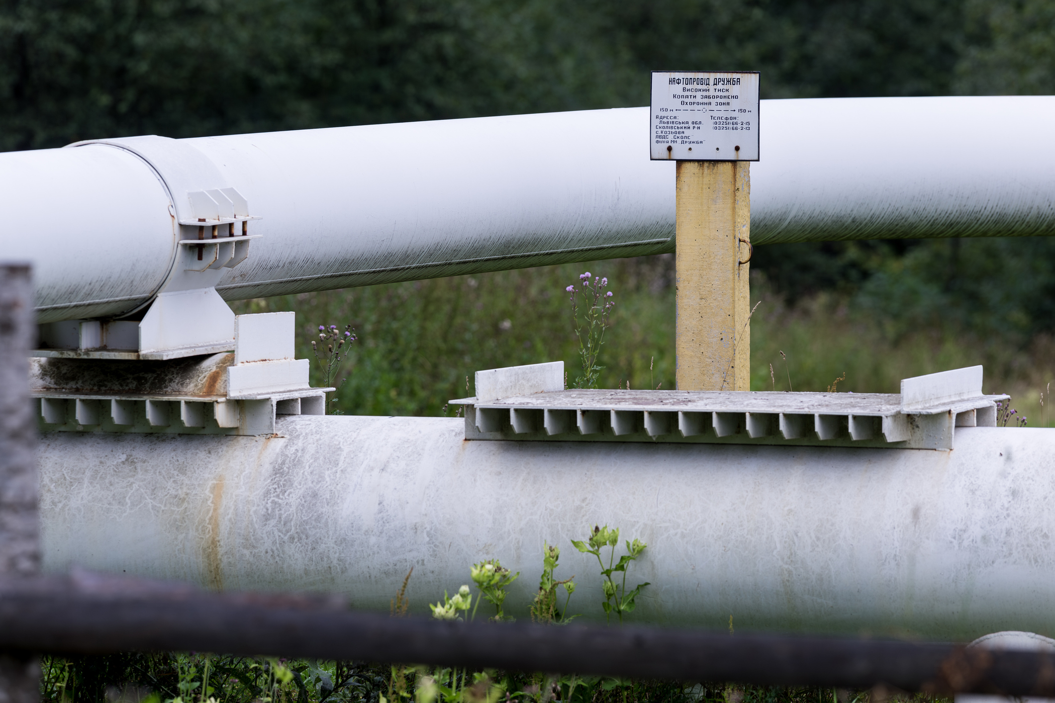 Kozyova, Ukraine Aug 14, 2013: Information board on a yellow pillar next to the Druzhba oil pipeline indicating the protection zone and emergency contact phone numbers for the site.