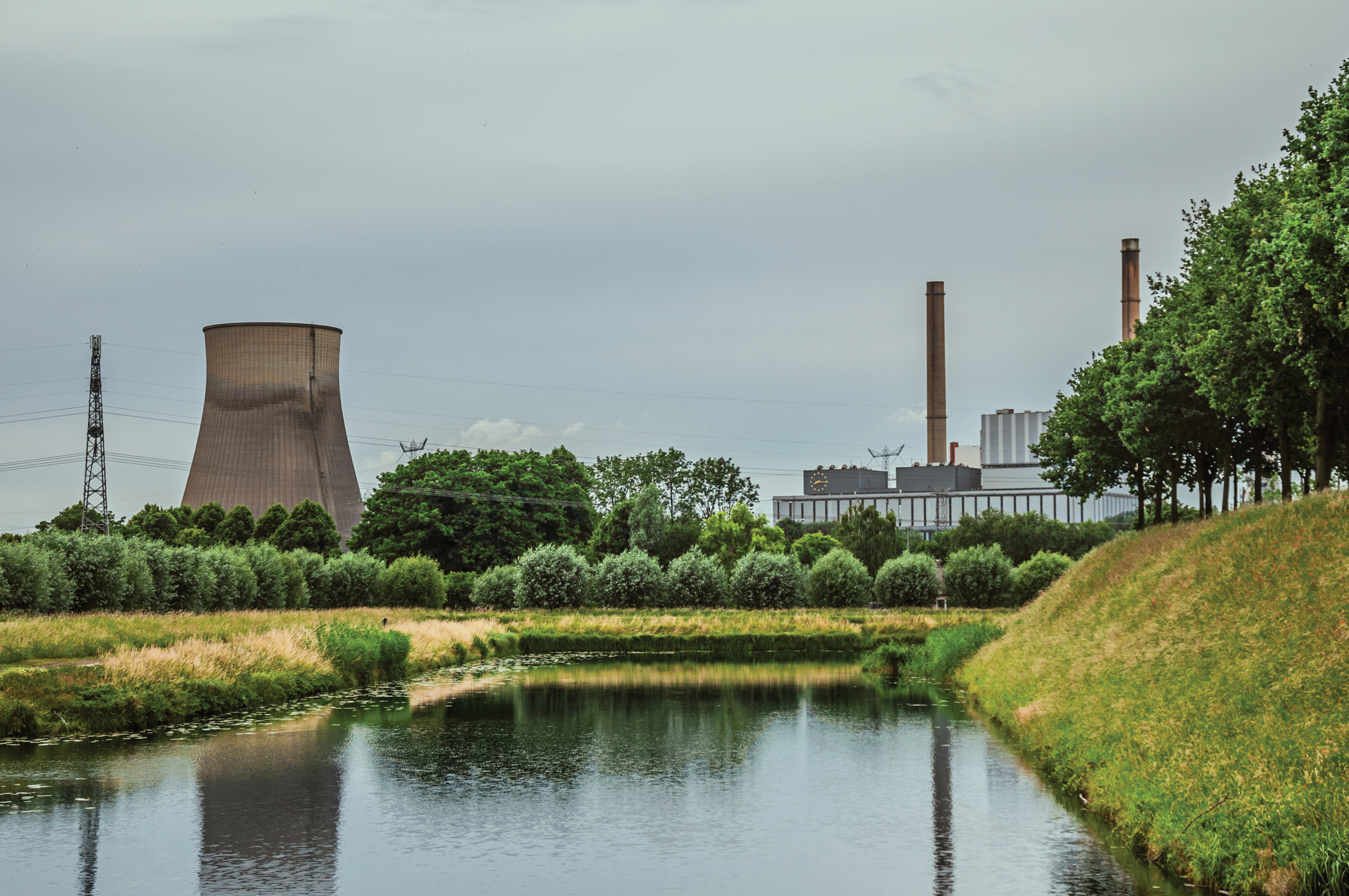 View of canal and gardens with nuclear power plant in background on cloudy day, near the village of Geertruidenberg. A small, friendly place near Aakvlaai Park and Breda. Southern Netherlands.